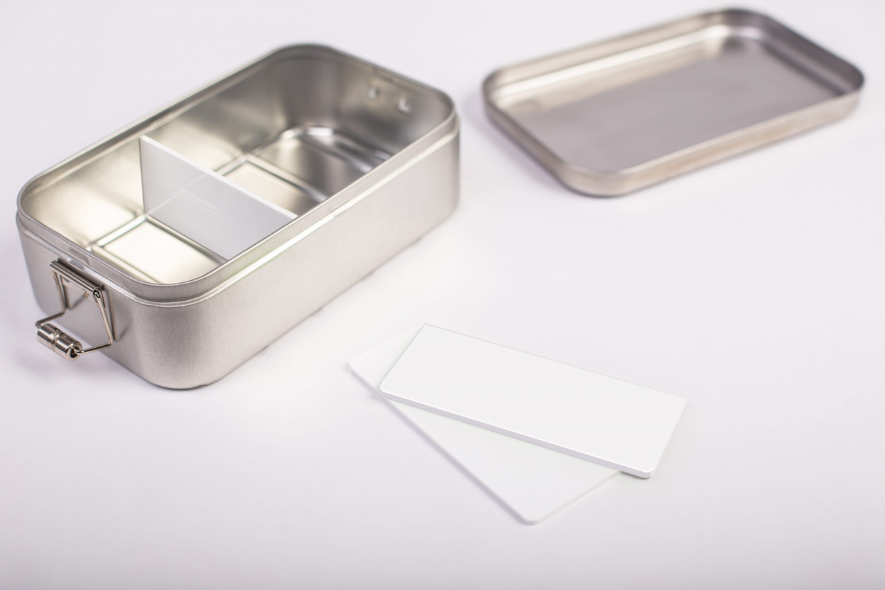 Offene Edelstahl-Lunchbox Classic Maxi mit eingesetzter weißer Trennwand; daneben zwei lose weiße Trennwände, Deckel separat im Hintergrund, neutraler Hintergrund.