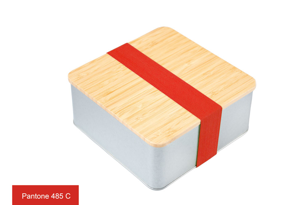 Quadratische Blechdose mit Bambusdeckel und rotem elastischem Band (Pantone 485 C) als Verschluss, auf weißem Hintergrund fotografiert.