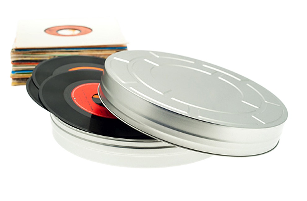 Geöffnete runde Filmdose XL aus silberfarbenem Metall mit abgenommenem Stülpdeckel, befüllt mit Schallplatten, daneben ein Stapel Schallplattenhüllen, auf weißem Hintergrund dargestellt.